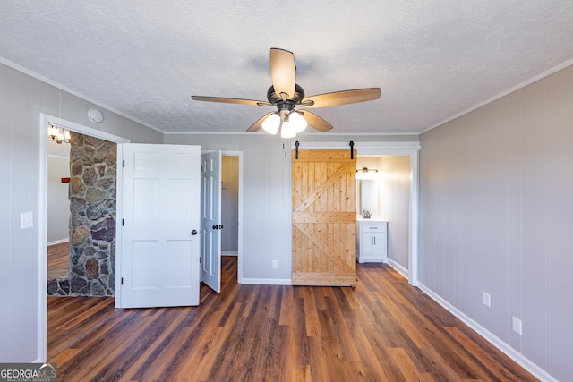 unfurnished bedroom featuring dark hardwood / wood-style floors, ornamental molding, a barn door, and a textured ceiling