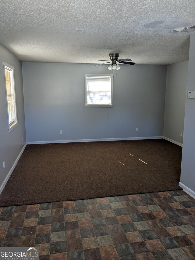 empty room featuring ceiling fan, a textured ceiling, and dark colored carpet