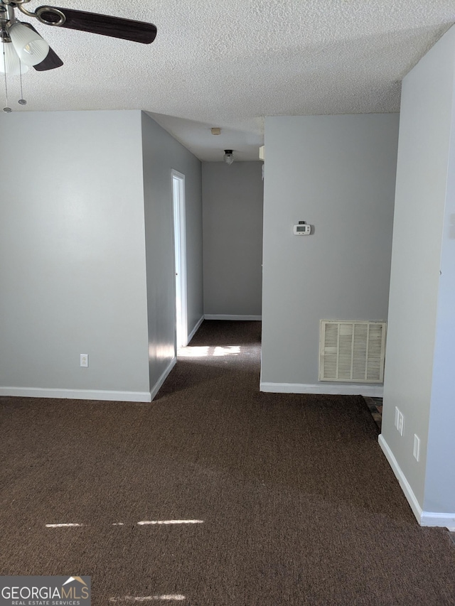 empty room featuring ceiling fan, dark carpet, and a textured ceiling