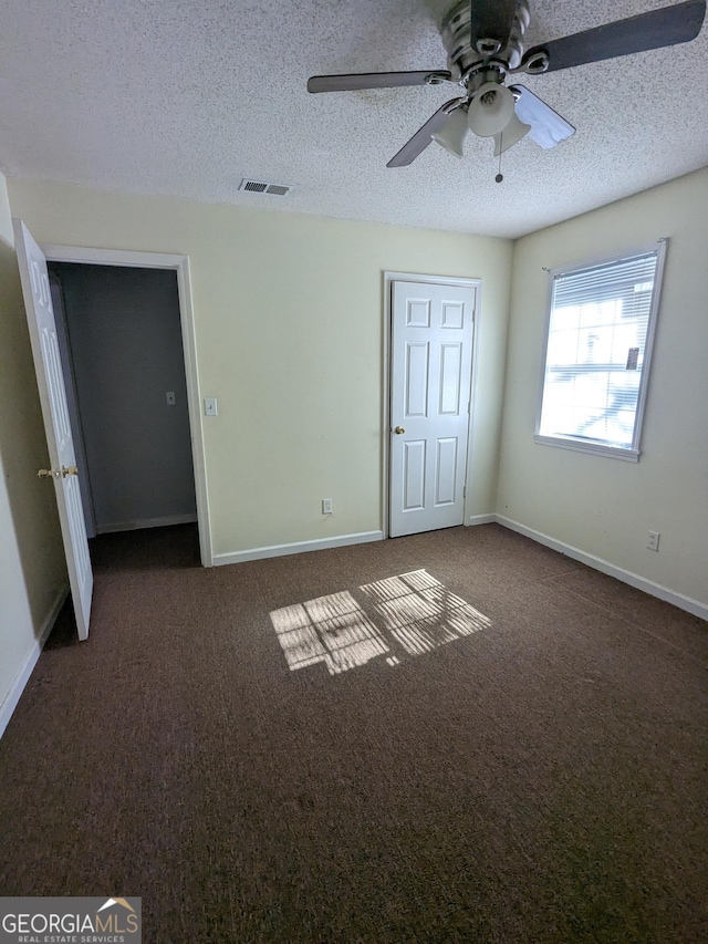 unfurnished bedroom with ceiling fan, dark carpet, and a textured ceiling