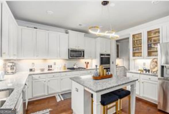 kitchen featuring white cabinetry, light stone counters, a center island, appliances with stainless steel finishes, and pendant lighting