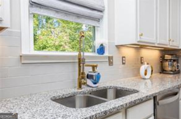 kitchen featuring sink, dishwasher, white cabinetry, light stone countertops, and decorative backsplash