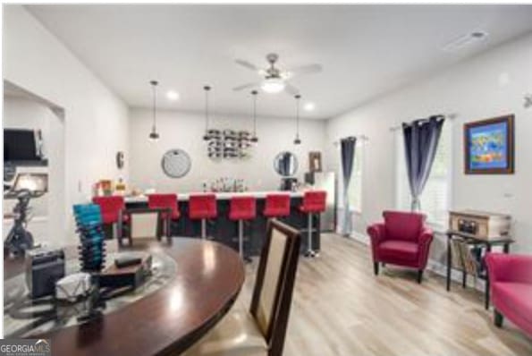 dining room with bar area, ceiling fan, and light hardwood / wood-style flooring