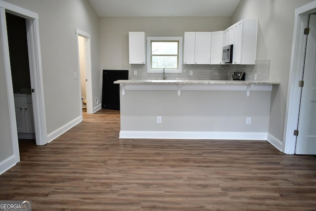 kitchen featuring white cabinetry, dark wood-type flooring, kitchen peninsula, and a kitchen bar