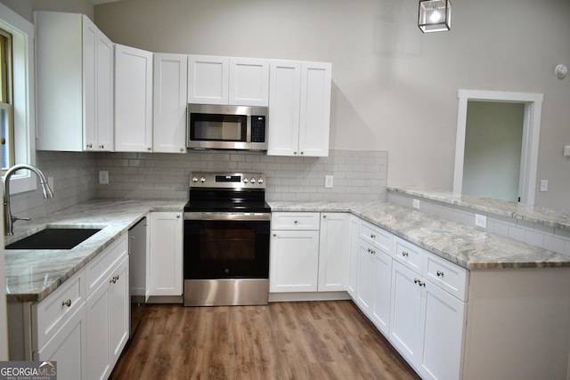 kitchen with tasteful backsplash, sink, white cabinets, kitchen peninsula, and stainless steel appliances