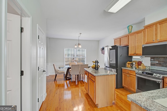 kitchen featuring light wood-style flooring, a kitchen island, appliances with stainless steel finishes, wainscoting, and light stone countertops