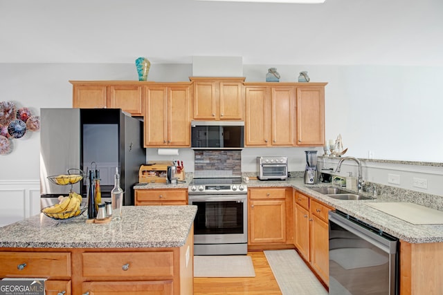 kitchen featuring light wood finished floors, stainless steel appliances, light brown cabinets, a sink, and a kitchen island