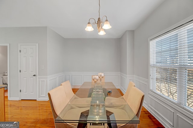 dining space with light wood finished floors, a decorative wall, a wainscoted wall, and an inviting chandelier