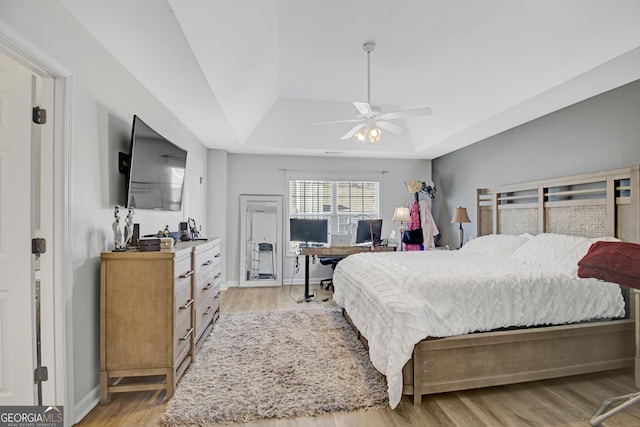 bedroom with a tray ceiling, light wood-style flooring, and baseboards