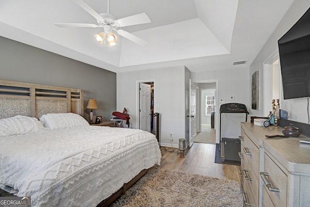 bedroom featuring baseboards, visible vents, a raised ceiling, ceiling fan, and light wood-style floors