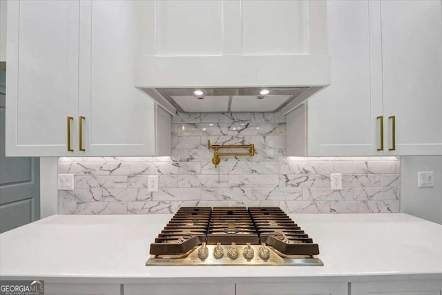 room details featuring tasteful backsplash, white cabinetry, stainless steel gas cooktop, and range hood