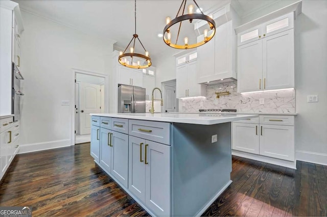 kitchen with pendant lighting, an island with sink, white cabinets, stainless steel fridge, and backsplash