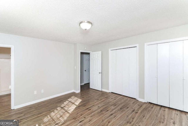 unfurnished bedroom featuring hardwood / wood-style flooring, multiple closets, and a textured ceiling