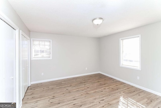 unfurnished bedroom with a closet, a textured ceiling, multiple windows, and light wood-type flooring