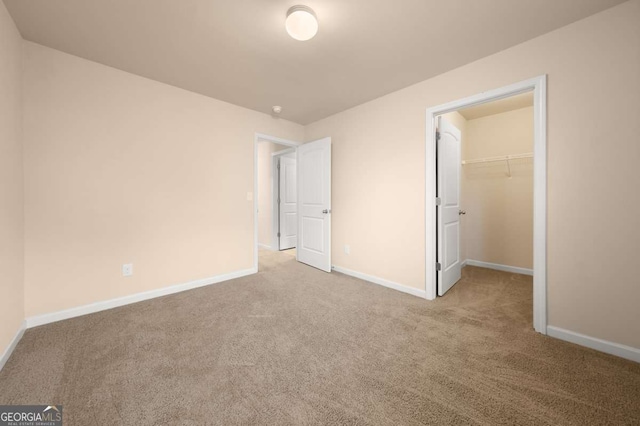 unfurnished bedroom with a spacious closet, light carpet, and a closet