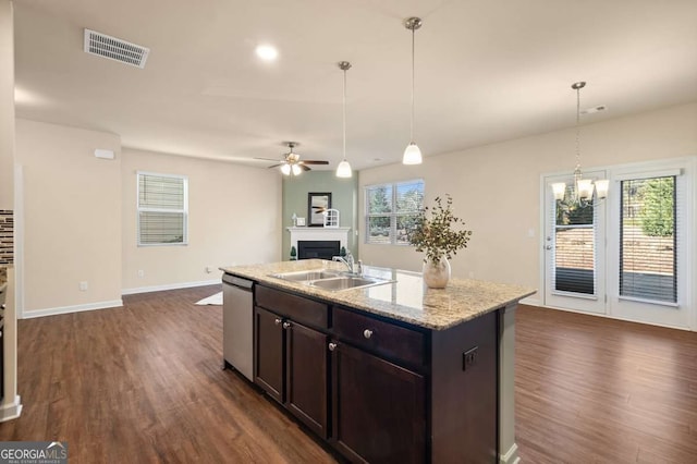 kitchen with an island with sink, light stone countertops, stainless steel dishwasher, and decorative light fixtures