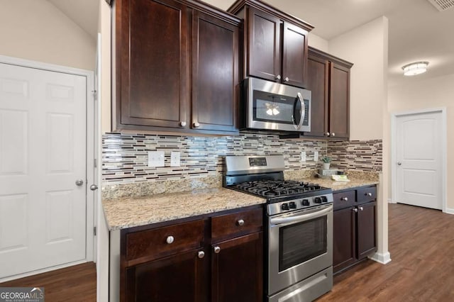 kitchen with dark wood-type flooring, backsplash, stainless steel appliances, dark brown cabinetry, and light stone countertops