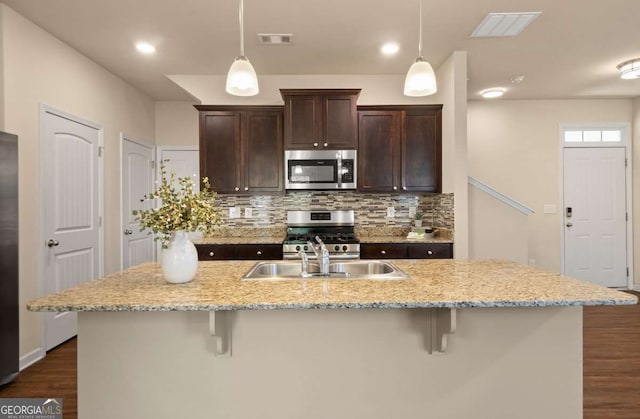 kitchen with stainless steel appliances, hanging light fixtures, a kitchen island with sink, and a breakfast bar area