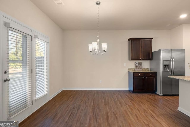 kitchen featuring dark wood-type flooring, dark brown cabinetry, light stone counters, stainless steel fridge, and pendant lighting