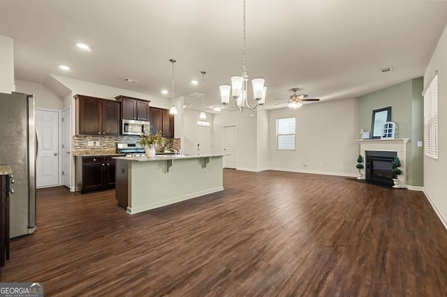 kitchen with a breakfast bar, appliances with stainless steel finishes, hanging light fixtures, dark brown cabinetry, and an island with sink