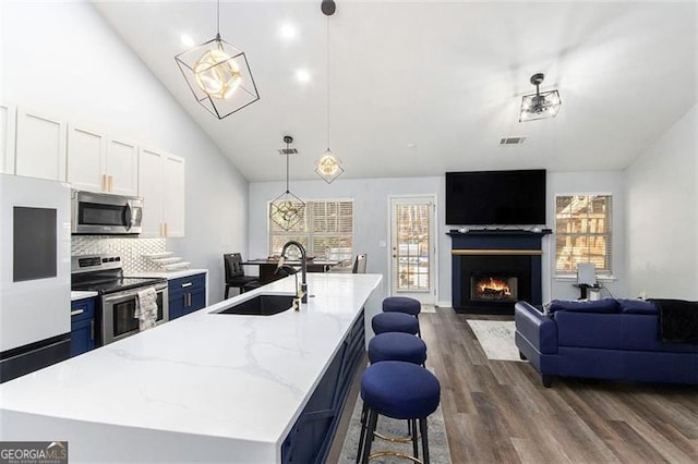 kitchen with appliances with stainless steel finishes, sink, a center island with sink, and decorative light fixtures