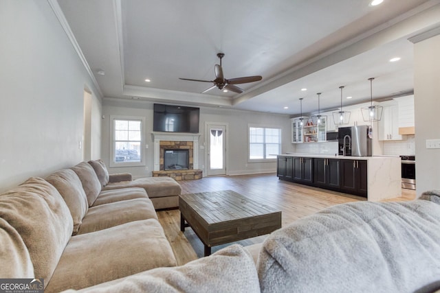 living room featuring plenty of natural light, a tray ceiling, light hardwood / wood-style floors, and a stone fireplace