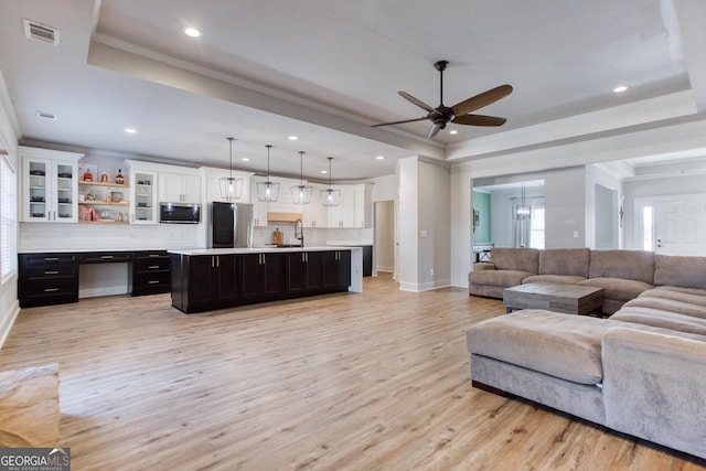 living room with ornamental molding, a raised ceiling, ceiling fan with notable chandelier, and light wood-type flooring