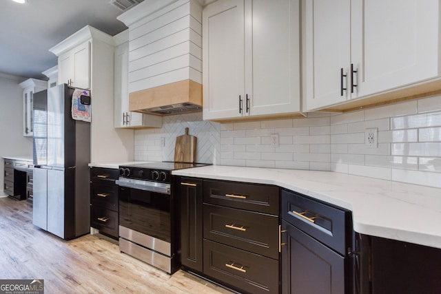 kitchen featuring stainless steel fridge, white cabinetry, electric range oven, light stone counters, and light wood-type flooring