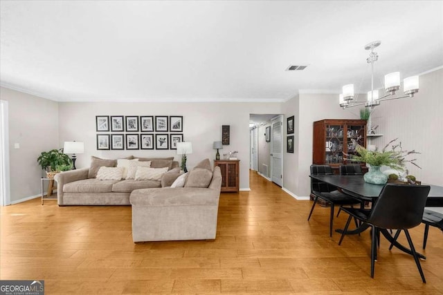 living room featuring a notable chandelier, ornamental molding, and light wood-type flooring