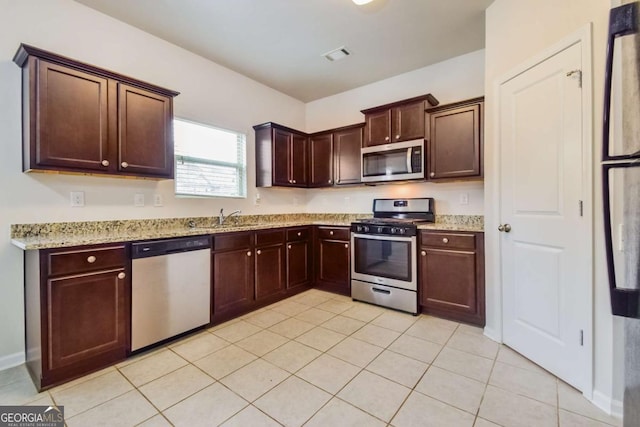 kitchen featuring appliances with stainless steel finishes, sink, light tile patterned floors, dark brown cabinetry, and light stone counters