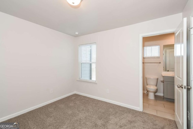 unfurnished bedroom featuring multiple windows, connected bathroom, and light carpet