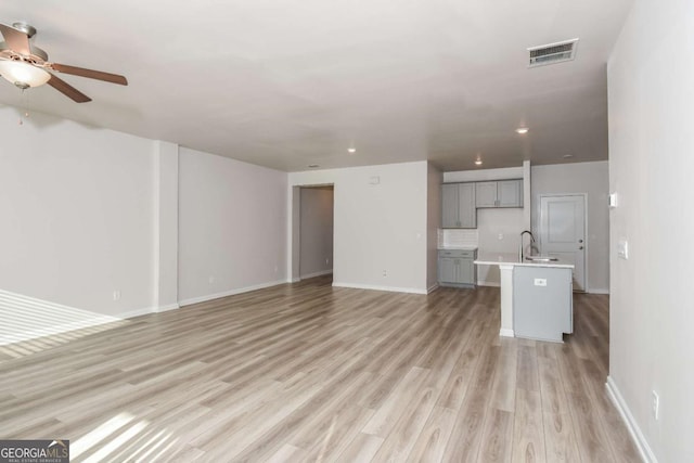 unfurnished living room with sink, light hardwood / wood-style floors, and ceiling fan