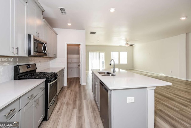 kitchen with an island with sink, sink, backsplash, light hardwood / wood-style floors, and stainless steel appliances