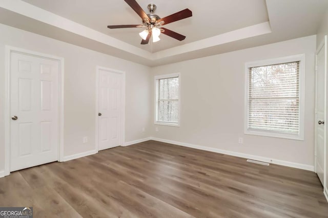 unfurnished bedroom with multiple windows, dark hardwood / wood-style floors, a raised ceiling, and ceiling fan