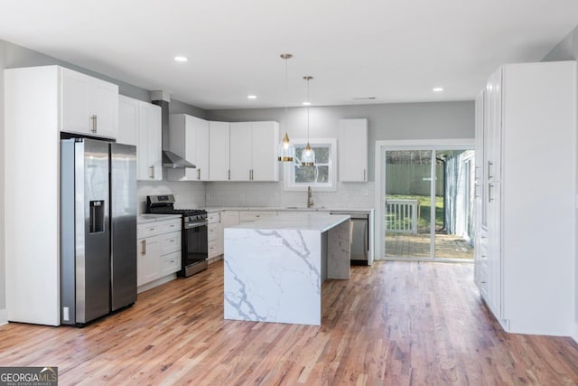 kitchen featuring white cabinetry, hanging light fixtures, stainless steel appliances, a center island, and wall chimney exhaust hood