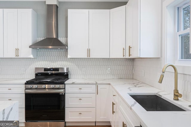 kitchen with wall chimney exhaust hood, sink, gas stove, white cabinetry, and backsplash