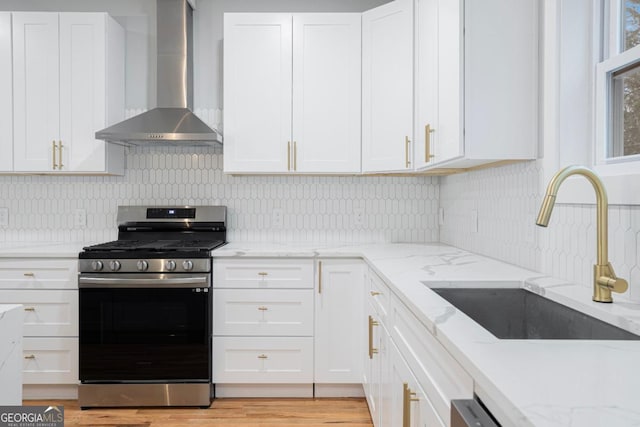 kitchen with white cabinetry, sink, backsplash, stainless steel gas range, and wall chimney exhaust hood