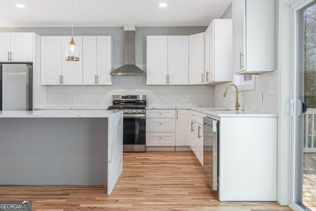 kitchen featuring sink, white cabinetry, decorative light fixtures, stainless steel appliances, and wall chimney range hood