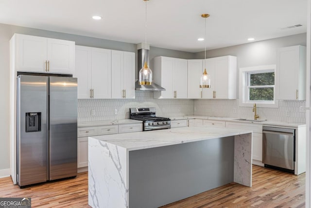 kitchen featuring wall chimney exhaust hood, sink, white cabinetry, pendant lighting, and stainless steel appliances