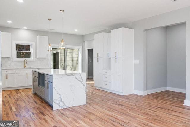 kitchen featuring white cabinetry, backsplash, hanging light fixtures, a center island, and light wood-type flooring