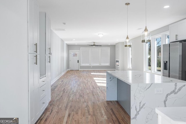 kitchen featuring stainless steel fridge, hanging light fixtures, a center island, light stone countertops, and white cabinets