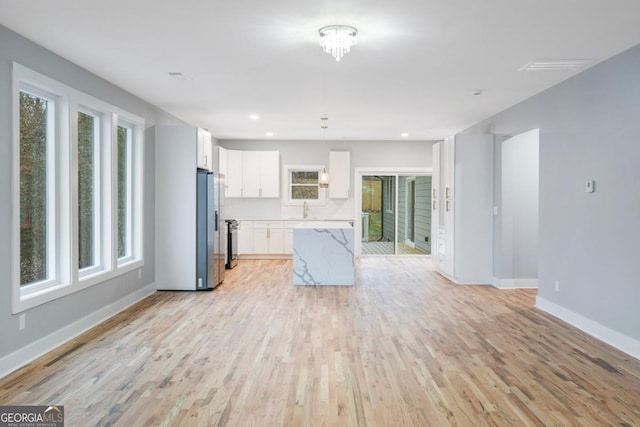 kitchen with stainless steel fridge with ice dispenser, white cabinetry, sink, light stone counters, and light hardwood / wood-style floors