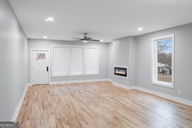 unfurnished living room featuring heating unit, a fireplace, ceiling fan, and light wood-type flooring