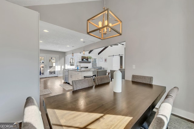 dining space with lofted ceiling, sink, an inviting chandelier, wood-type flooring, and a barn door