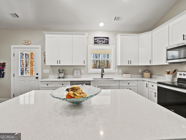 kitchen featuring lofted ceiling, sink, white cabinetry, light stone counters, and appliances with stainless steel finishes