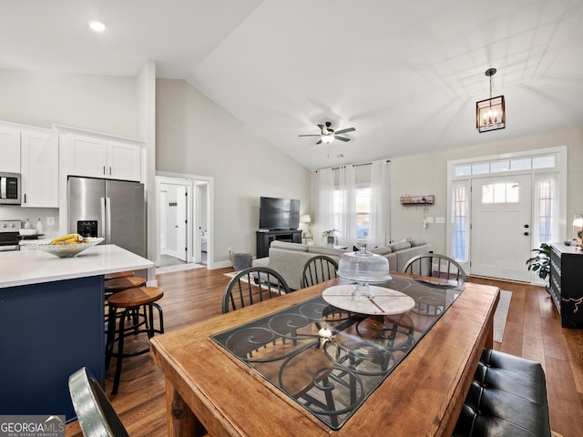 dining space with dark wood-type flooring, ceiling fan with notable chandelier, and high vaulted ceiling