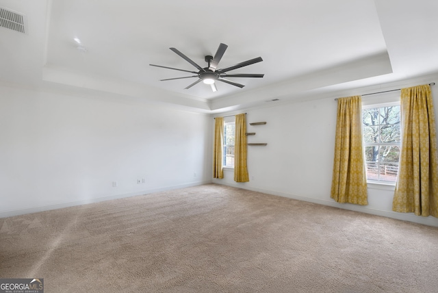 carpeted spare room with a raised ceiling, a healthy amount of sunlight, and ceiling fan