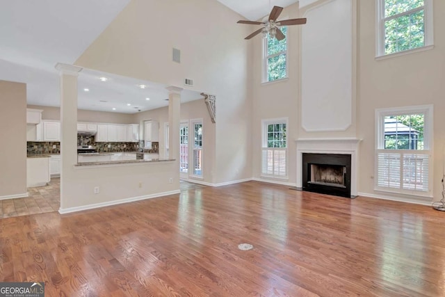 unfurnished living room with ceiling fan, plenty of natural light, light wood-type flooring, and ornate columns