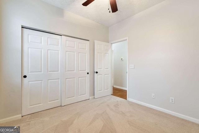 unfurnished bedroom featuring ceiling fan, light colored carpet, a closet, and a textured ceiling