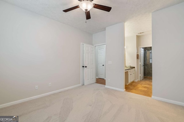 unfurnished bedroom with ceiling fan, light colored carpet, ensuite bath, and a textured ceiling